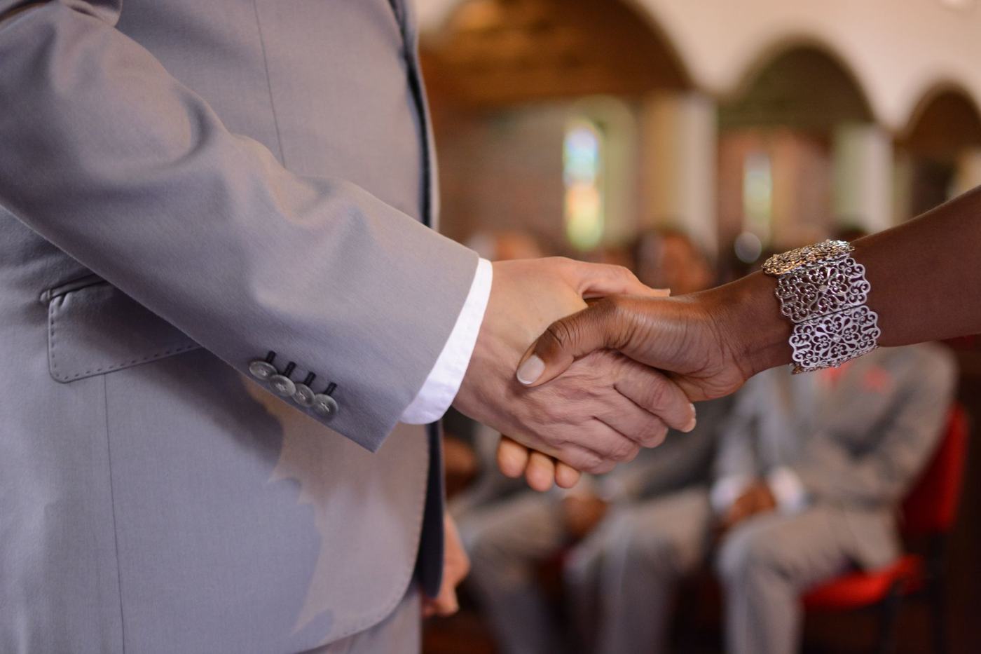 A close-up of an elegant handshake during a formal ceremony indoors, focusing on attire and jewelry.